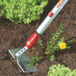 WOLF-Garten HWM15 Multi-Change® Draw Hoe with red and yellow 15cm steel head and swan-neck arm, shown on a bed of soil by a weed